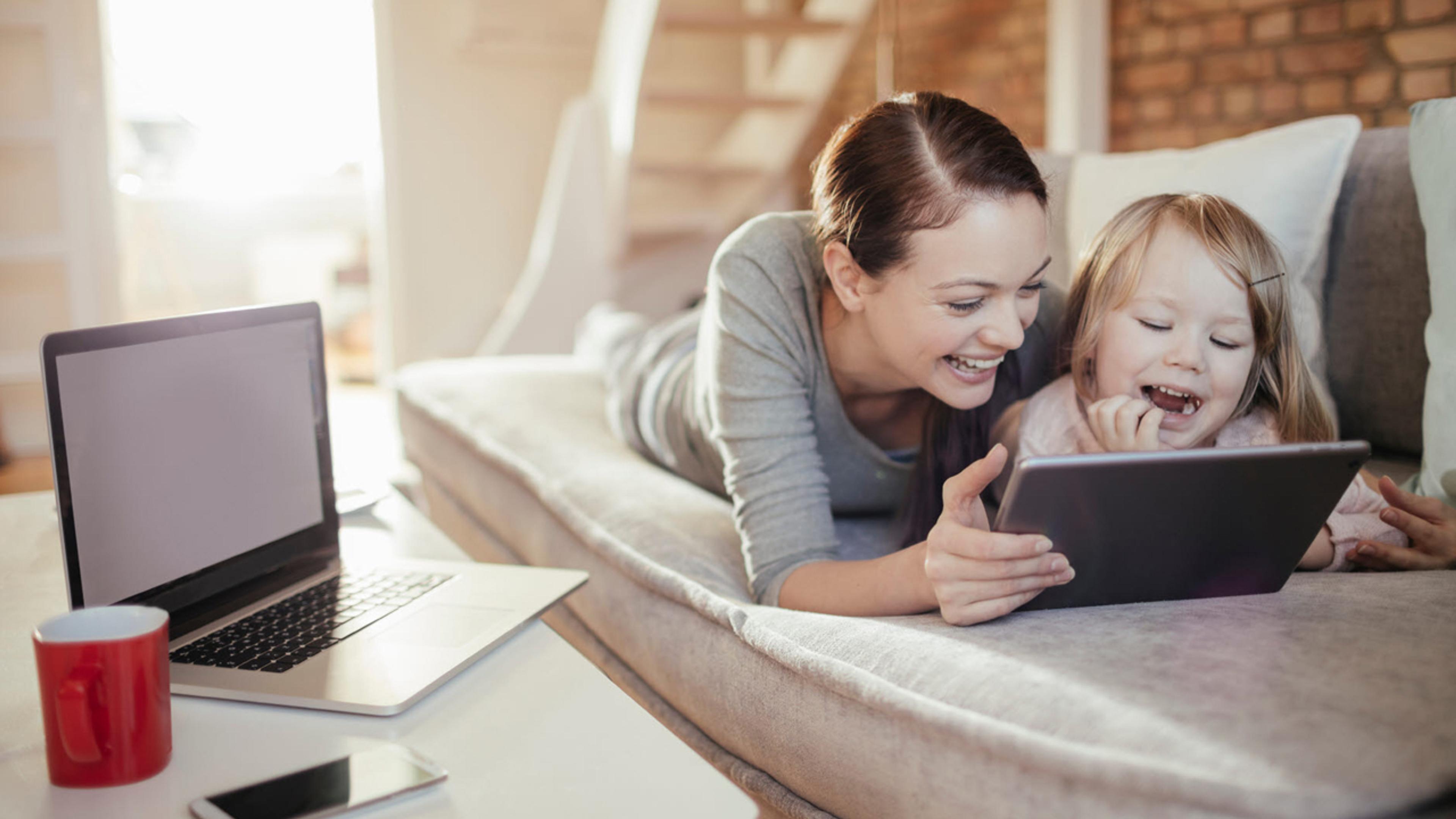Kvinne og barn ser på iPad på sofaen.