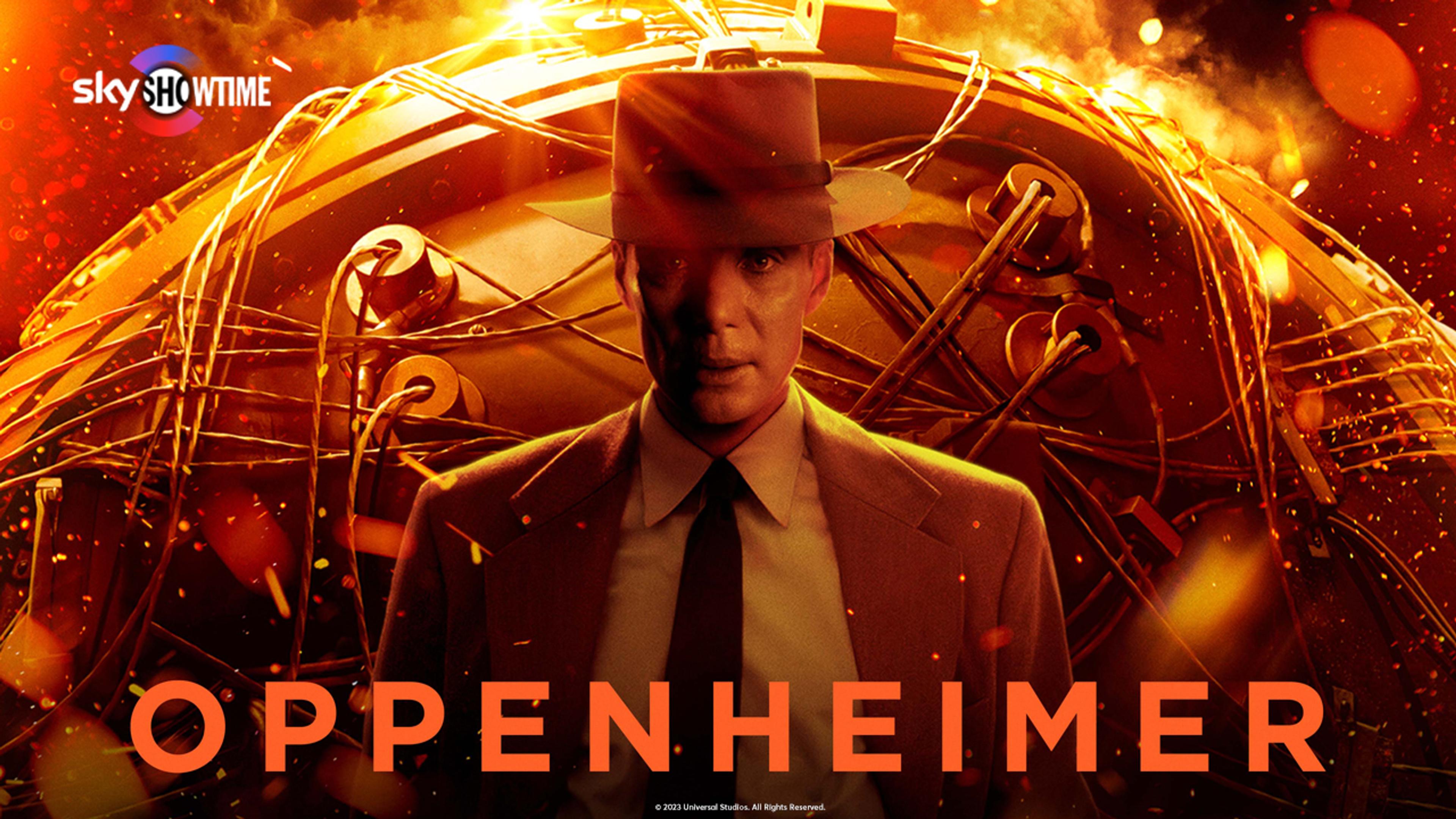 En mann i dress og hatt står foran en gigantisk atombombe med flammer rundt.