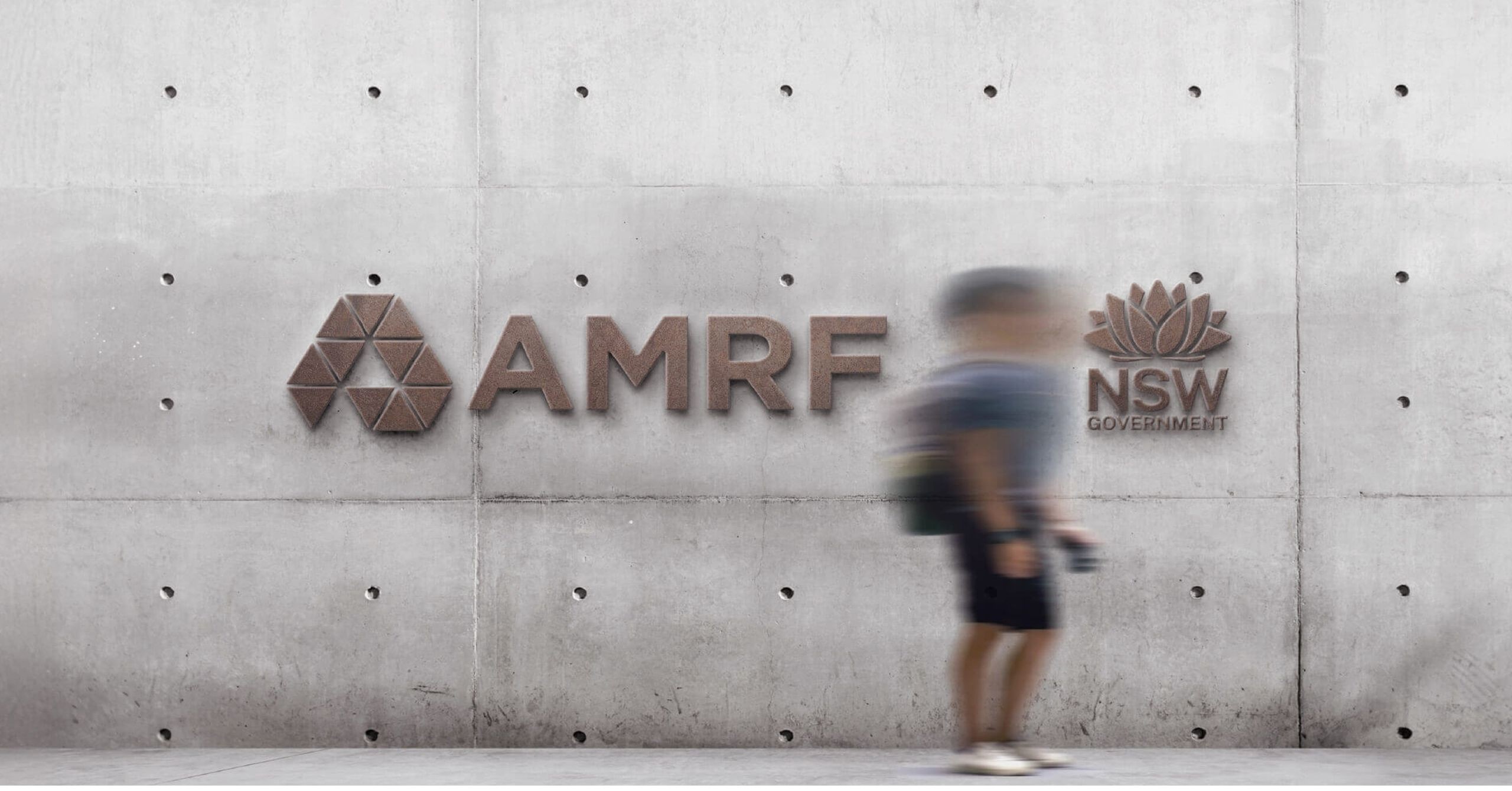 AMRF logo signage mounted on a concrete wall with a person walking past.