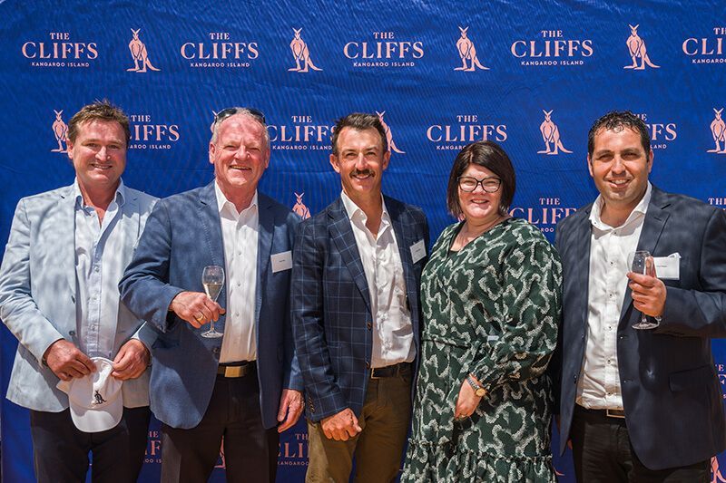Five guests posing in front of The Cliffs branded media wall at the Kangaroo Island launch event.