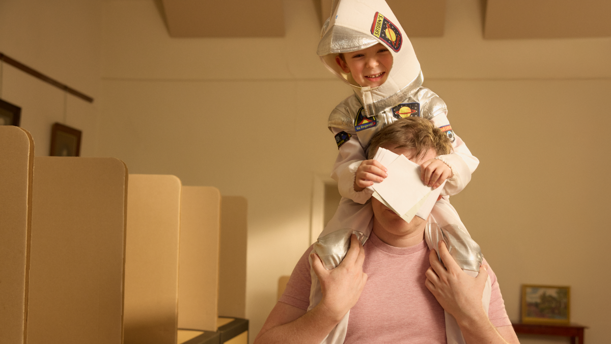 Child dressed as an astronaut sitting on persons shoulders