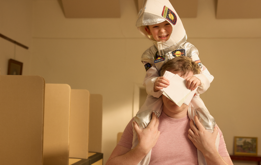 Child dressed as an astronaut sitting on persons shoulders