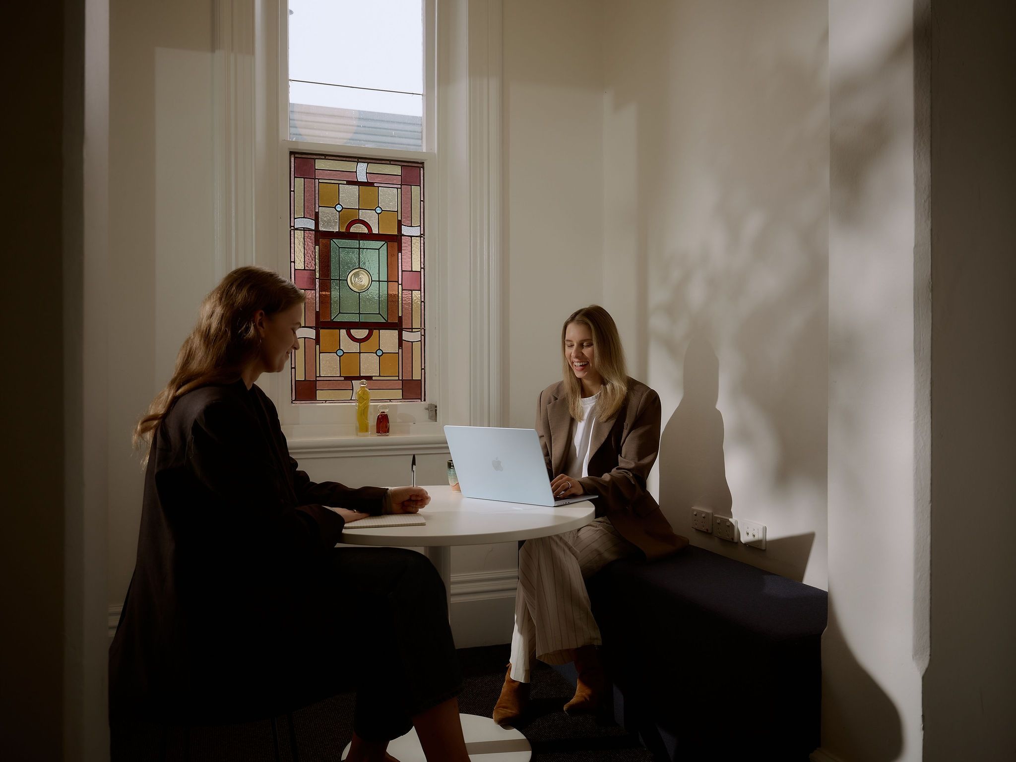 Rachael and Nadia sitting around a table with a stained glass window in the background
