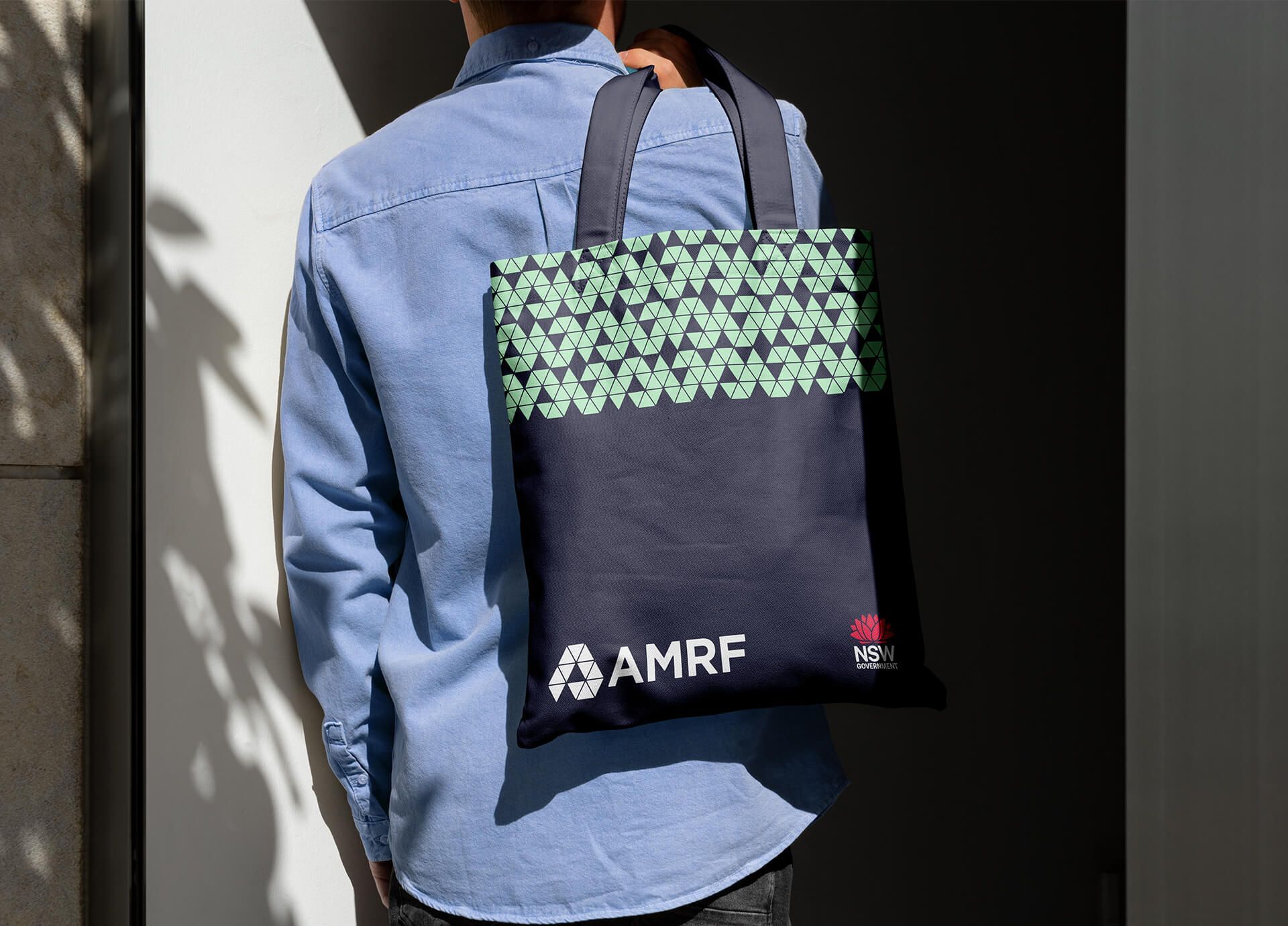 Person carrying an AMRF branded navy tote bag with a green geometric pattern.