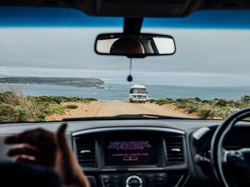 View from inside a car looking out the windscreen at a van and the ocean in the background