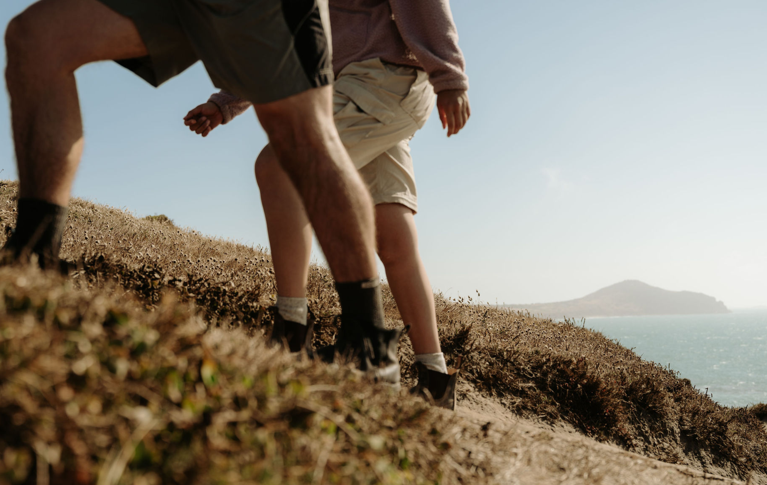 Two people walking through coastal scrub during filming for “The Coast is Calling” campaign.