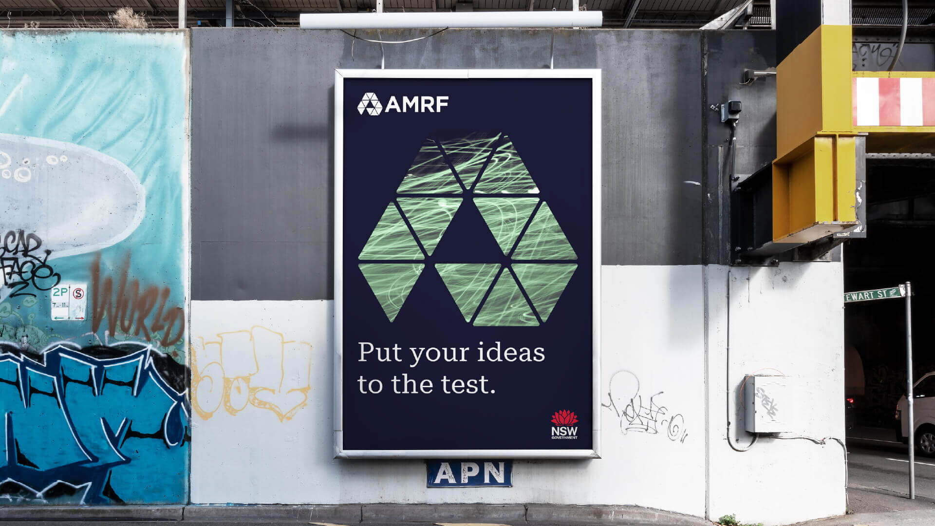 AMRF campaign billboard featuring geometric green artwork and the message “Put your ideas to the test.”