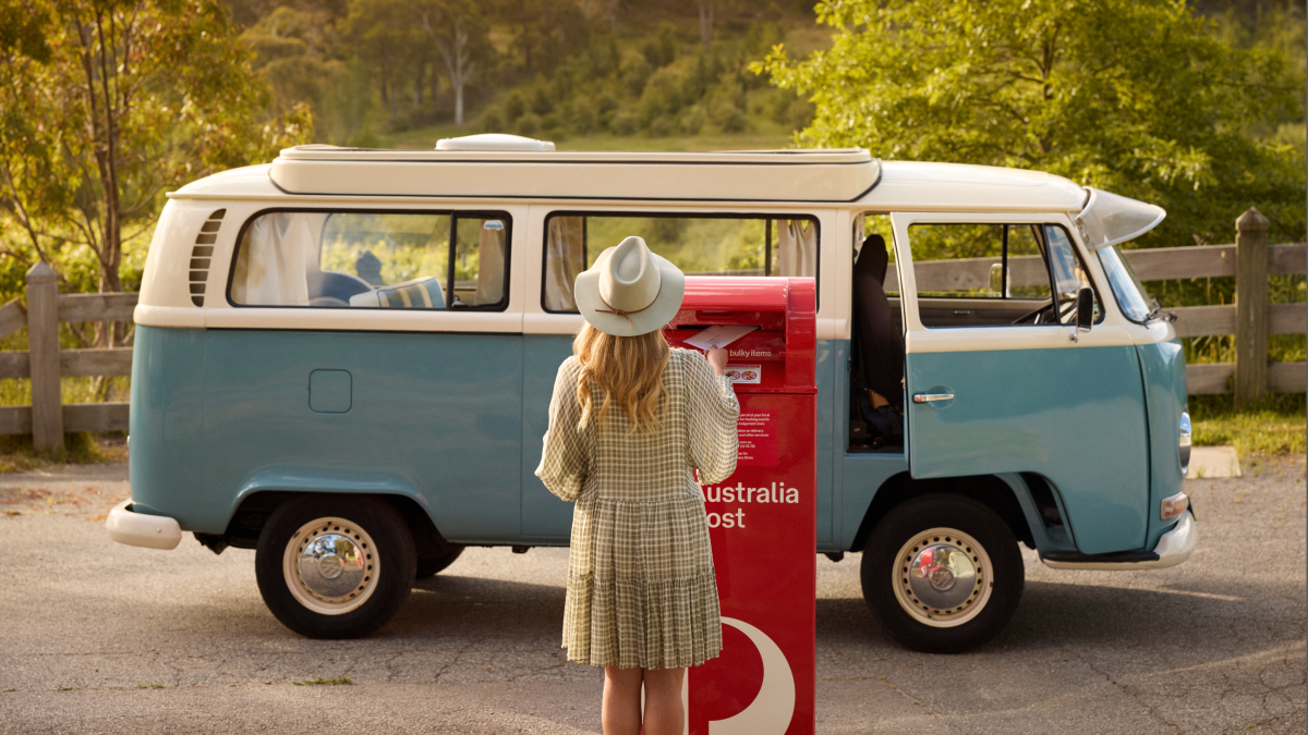 a person placing a vote in an australia post box in front of a van
