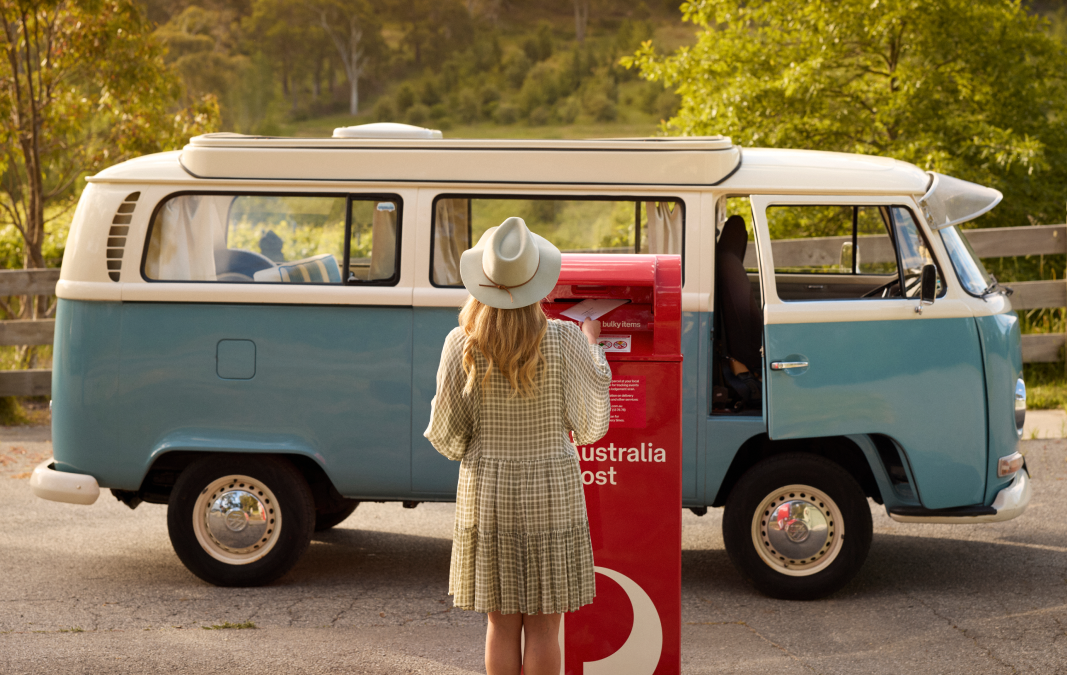 a person placing a vote in an australia post box in front of a van