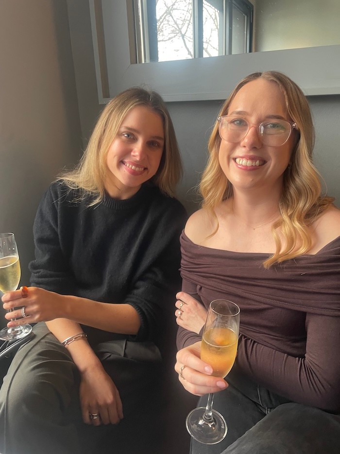 Nadia and Holly holding drinks smiling to camera