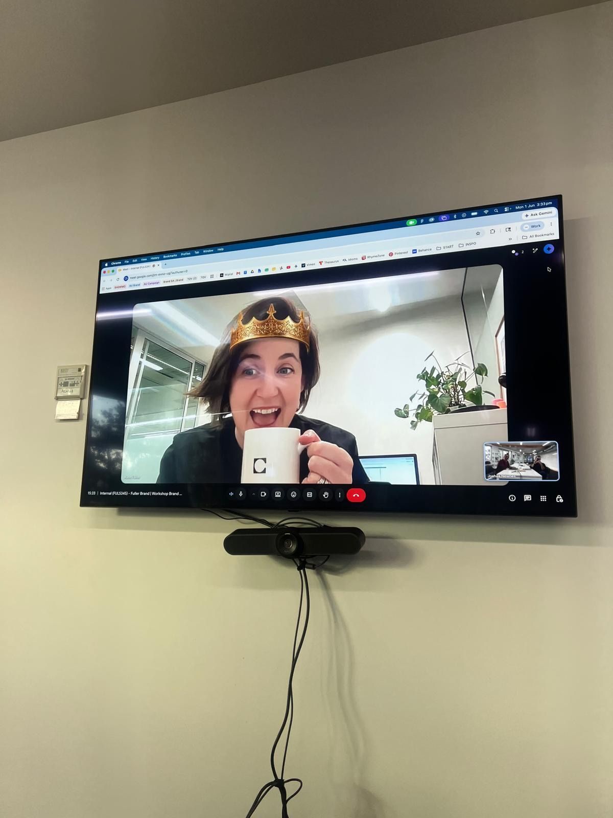 Kate holding a coffee cup with a crown on her head on a screen in a boardroom tv