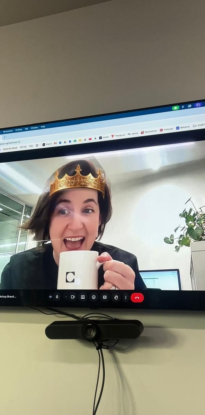 Kate holding a coffee cup with a crown on her head on a screen in a boardroom tv