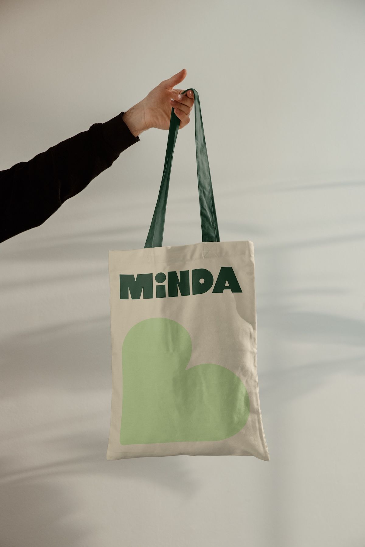Arm in frame holding up a tote bag with Minda branding and a love heart