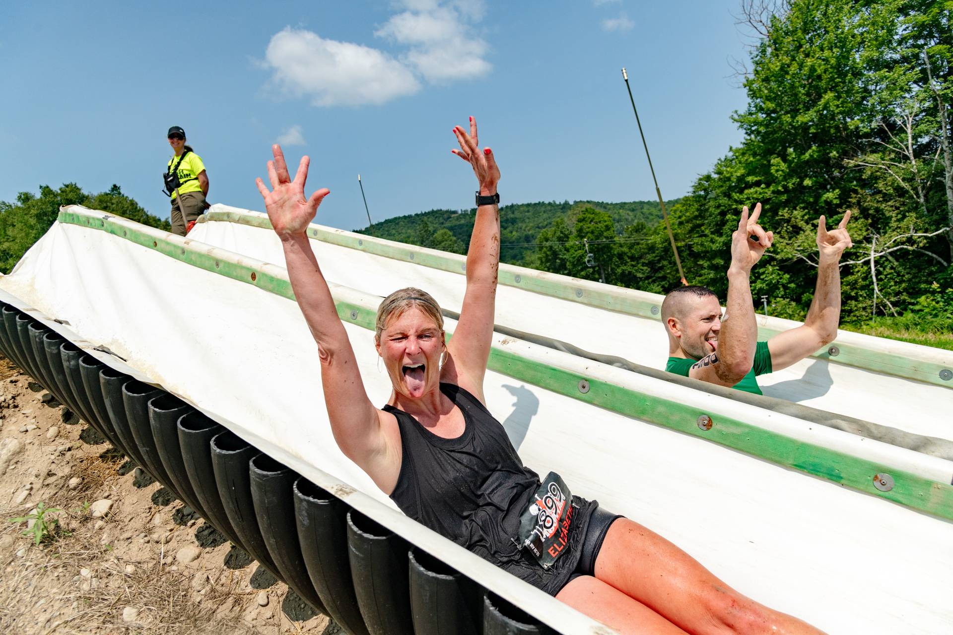 A man and a woman going down a slide, with their hands in the air, at Sunday River's Tough Mountain Challenge.