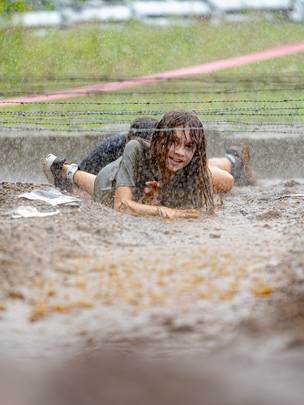 Tough Mountain Challenge competitor crawling through mud.