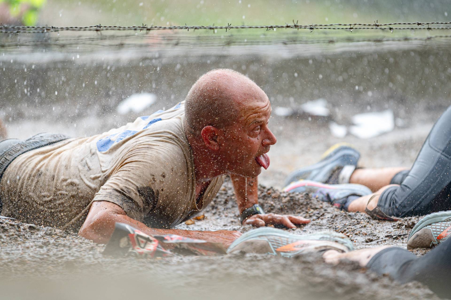 A man with his tongue out crawling through mud at the Tough Mountain Challenge.