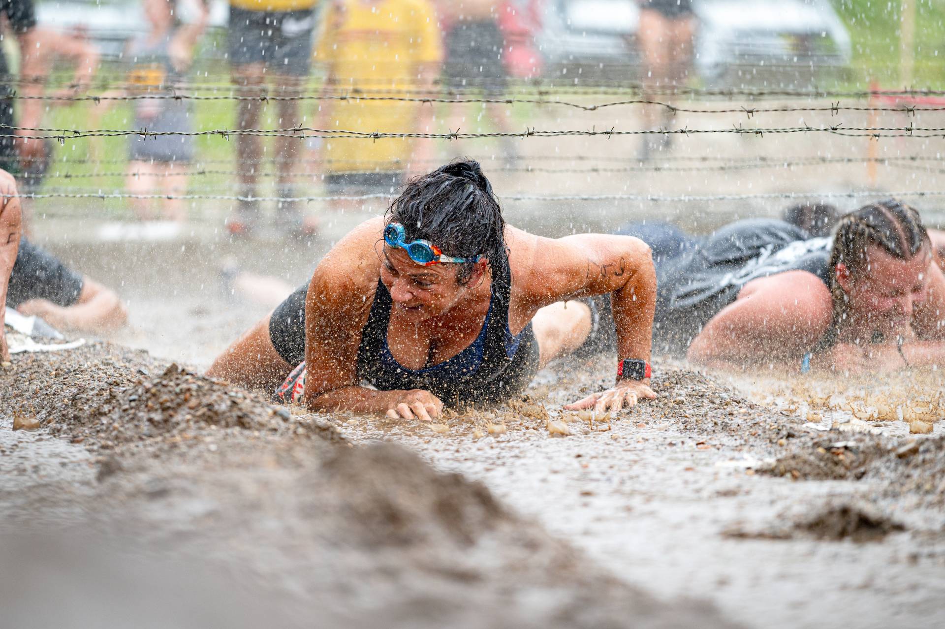 TMC participant crawling through the mud under barbed wire.