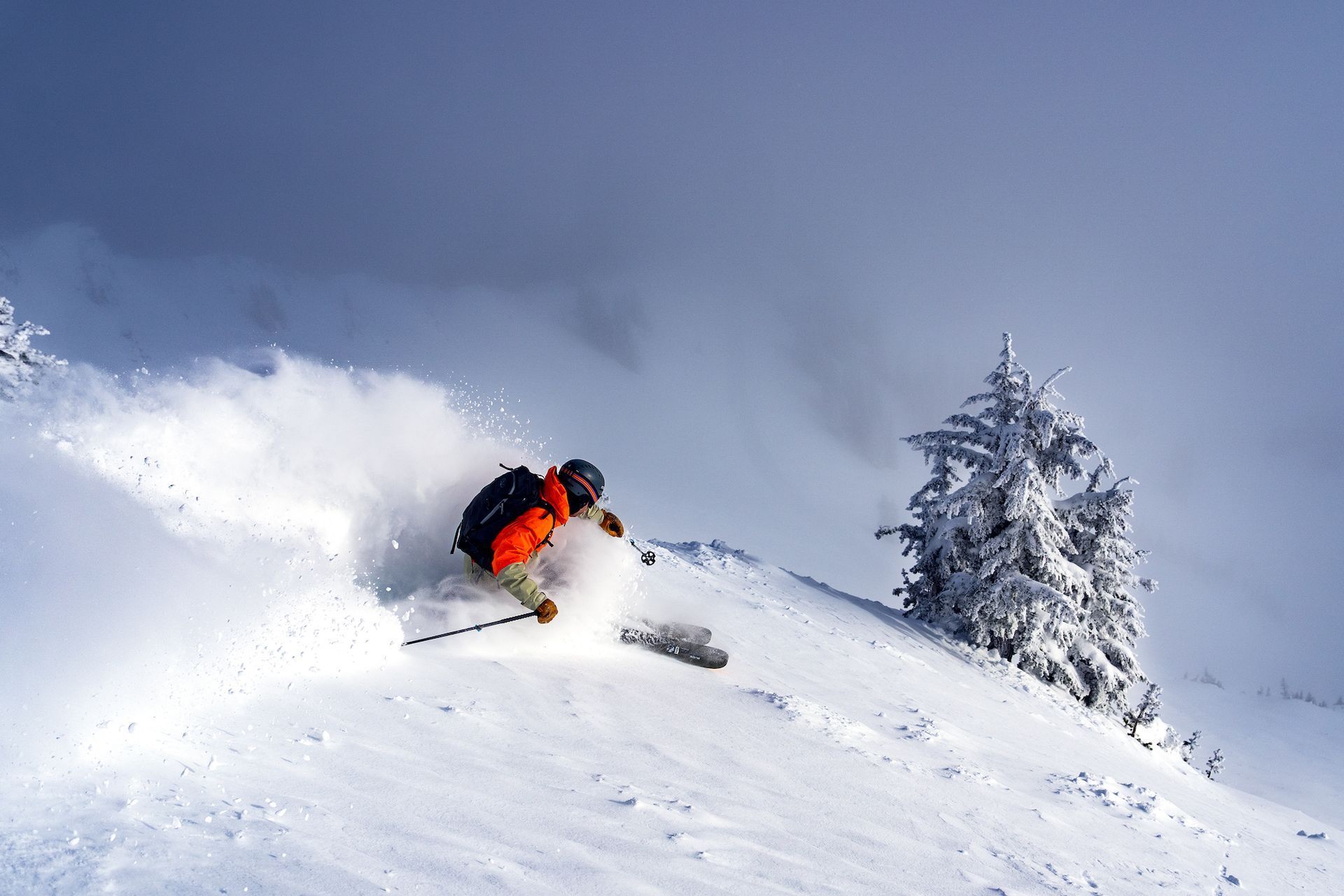 Lone skier on a semi-steep ridge turns into untouched powder underneath a shining sun and bluebird sky. 
