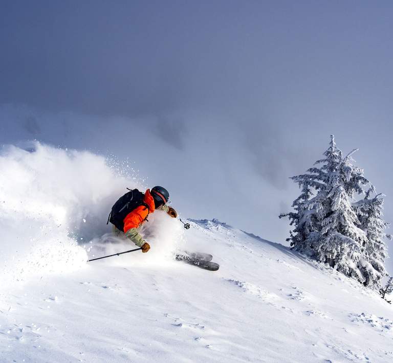 Lone skier on a semi-steep ridge turns into untouched powder underneath a shining sun and bluebird sky.