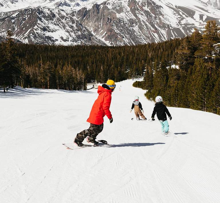 One adult and two children snowboard downhill.