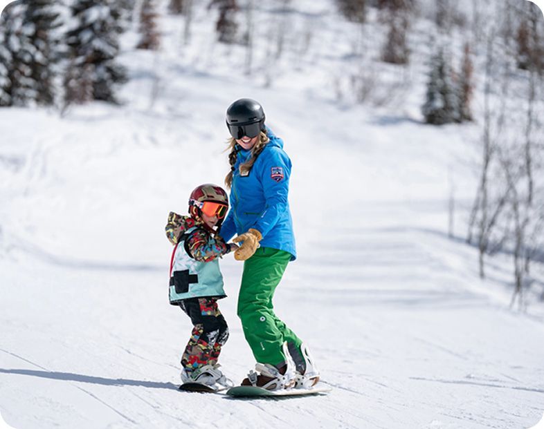 Adult teaching child how to snowboard