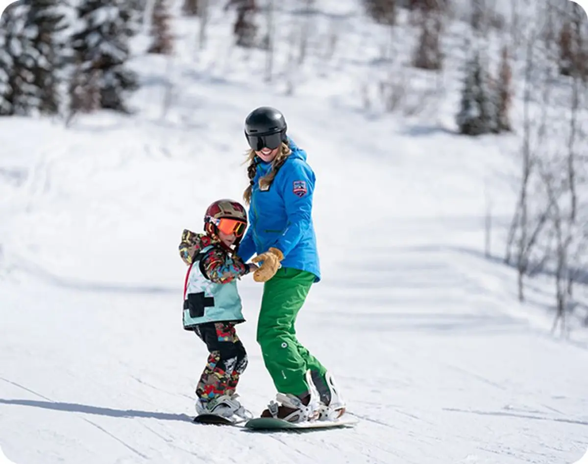 Adult teaching child how to snowboard