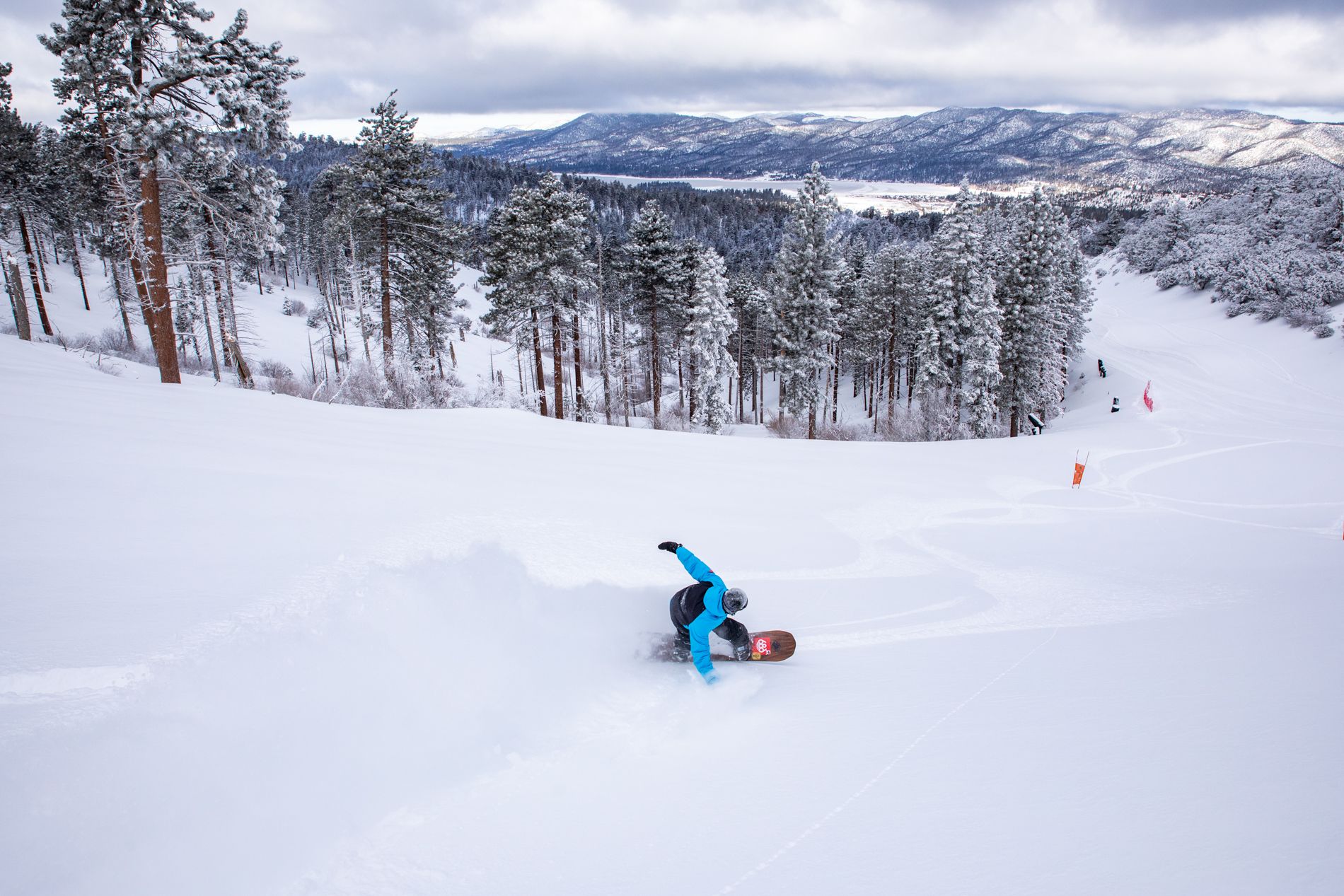 Snowboarder headed downhill with a cloud of powder spraying behind them.