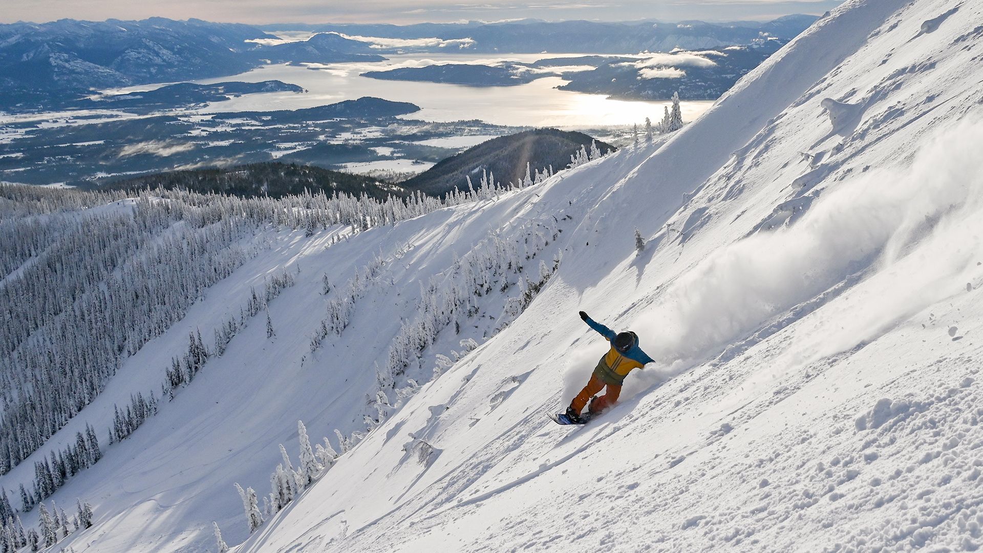 snowboarder riding fresh powder on a sunny day with lake in background