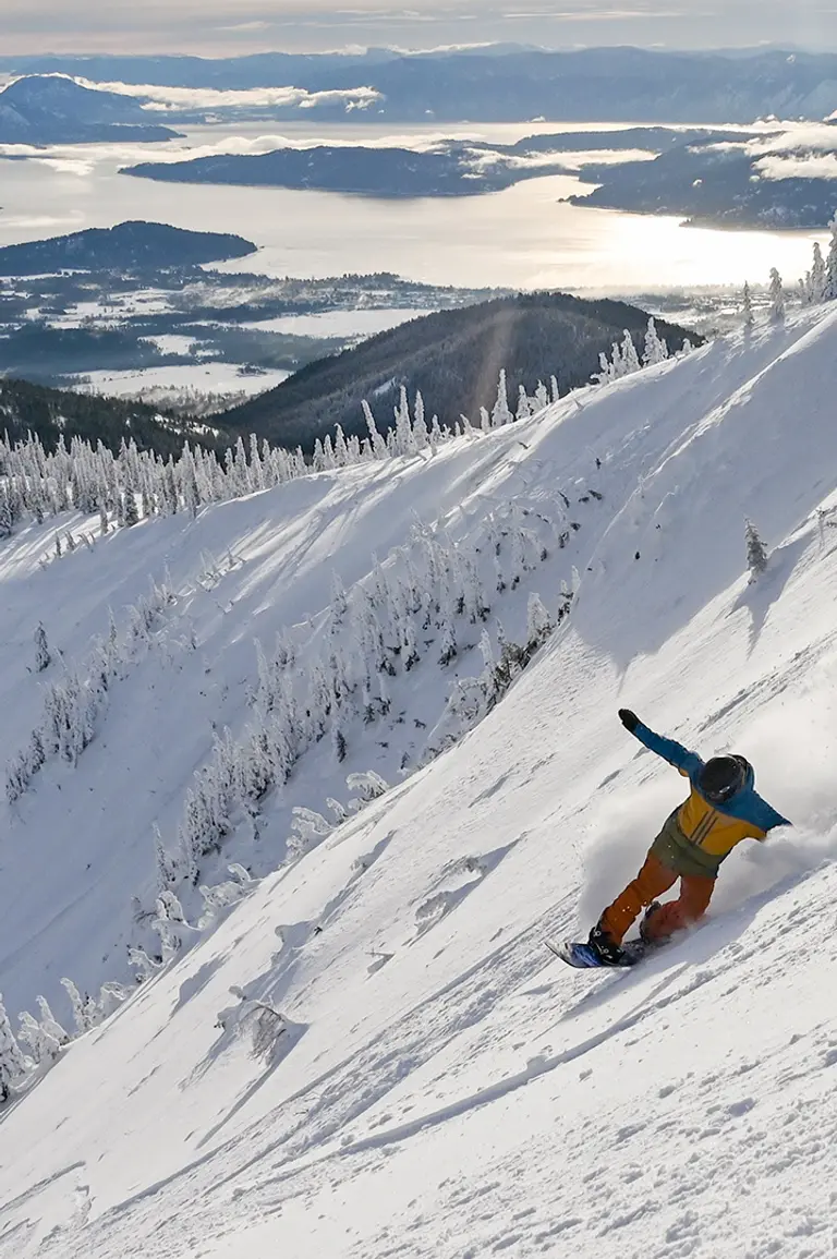 snowboarder riding fresh powder on a sunny day with lake in background