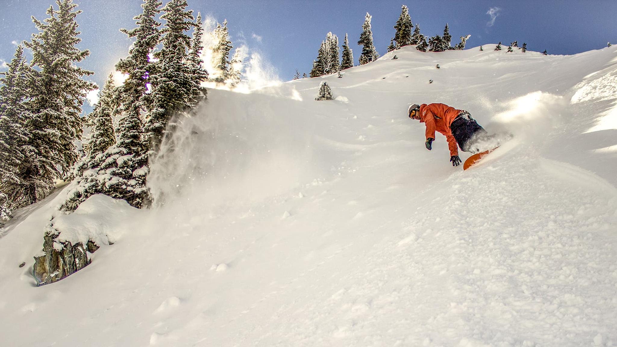 Snowboarder carving down a steep mountain slope.