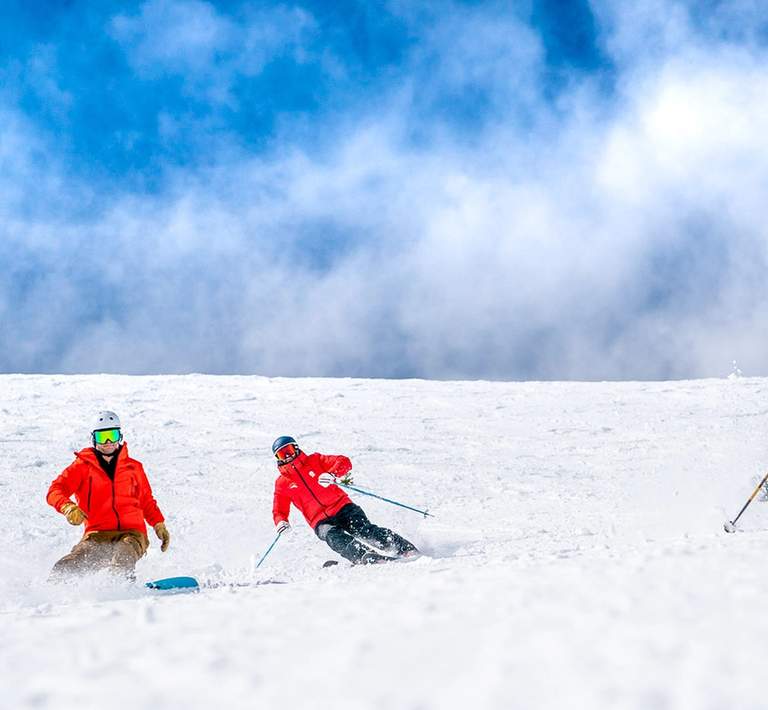 Person in snow gear holding a snowboard at the top of a snowy mountain