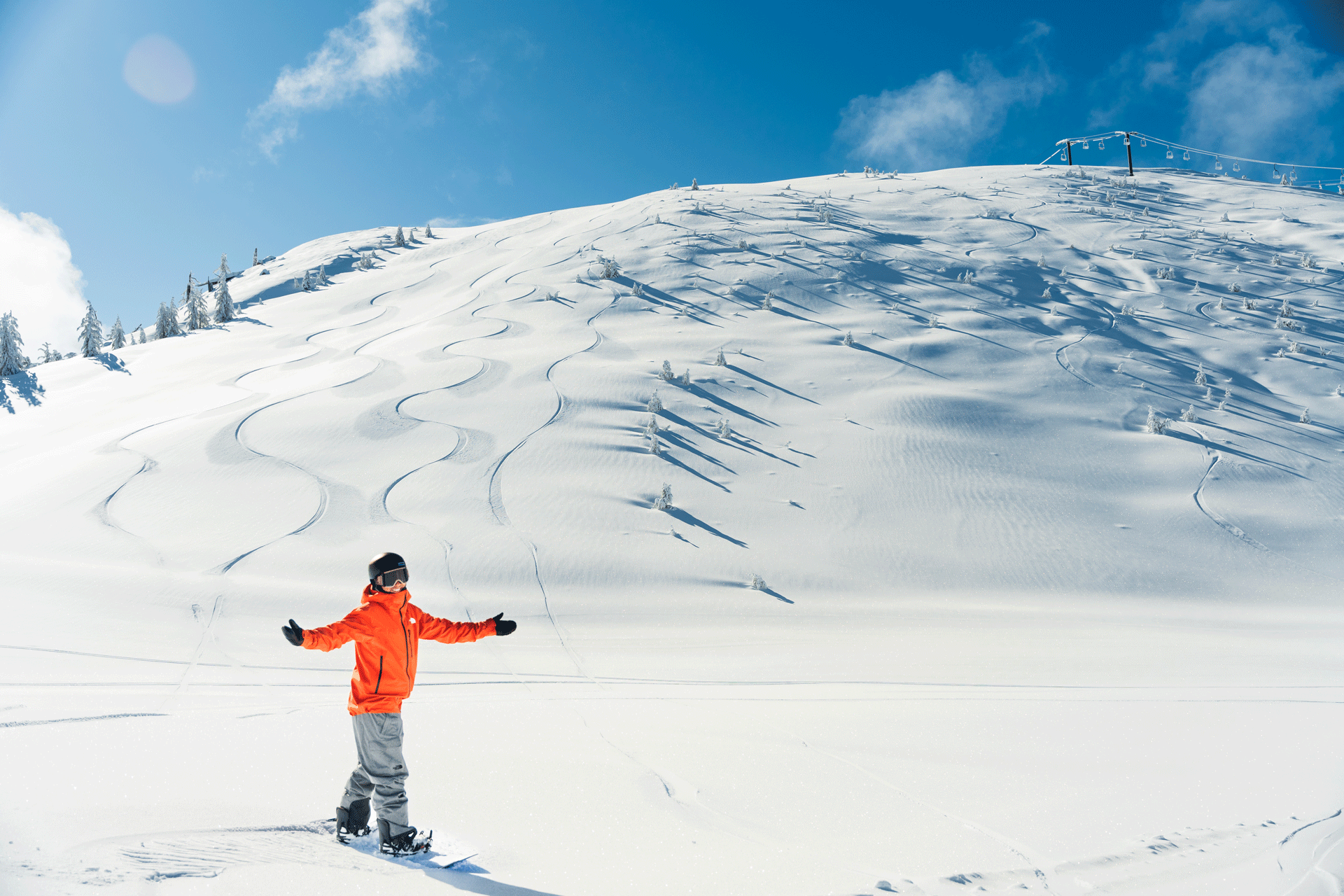 Snowboarder wearing an orange jacket standing at the bottom of Slide Peak at Snow Valley in the wintertime