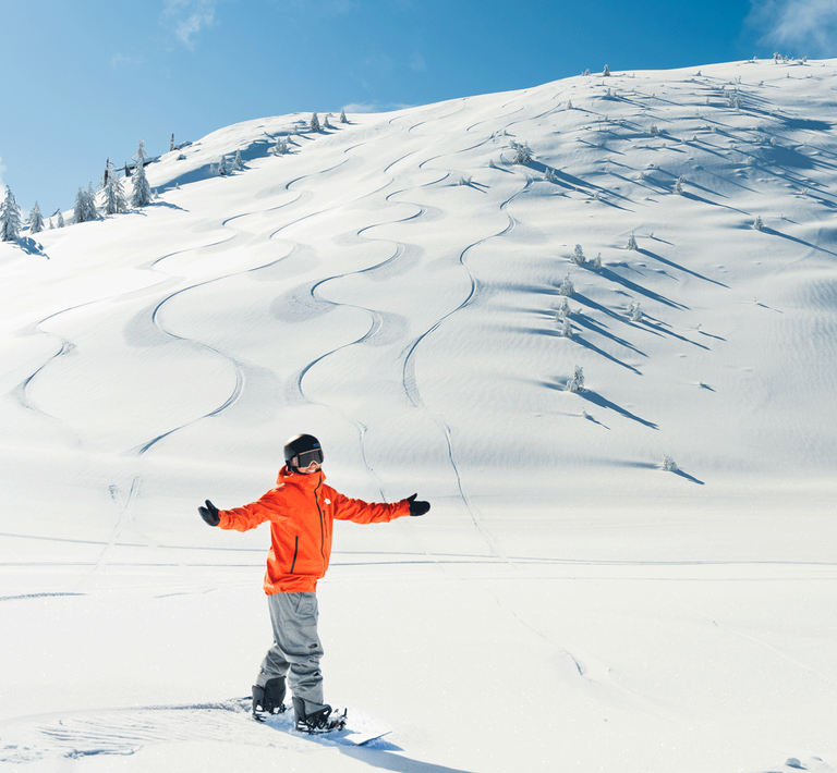 Snowboarder wearing an orange jacket standing at the bottom of Slide Peak at Snow Valley in the wintertime