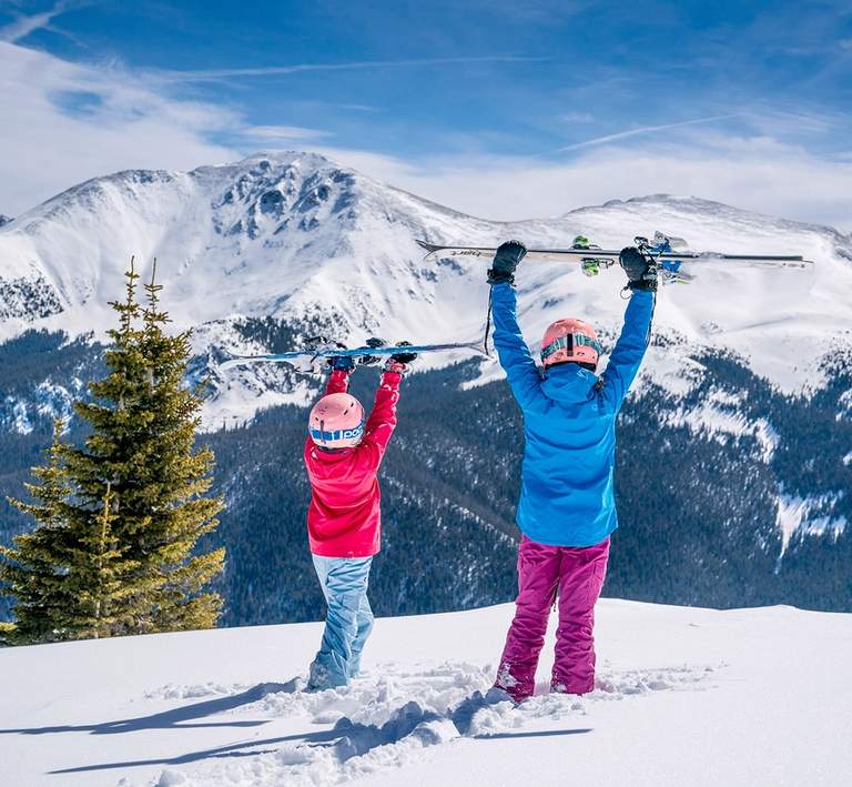 Two children holding skis overhead on top of mountain at Winter Park Ski resort