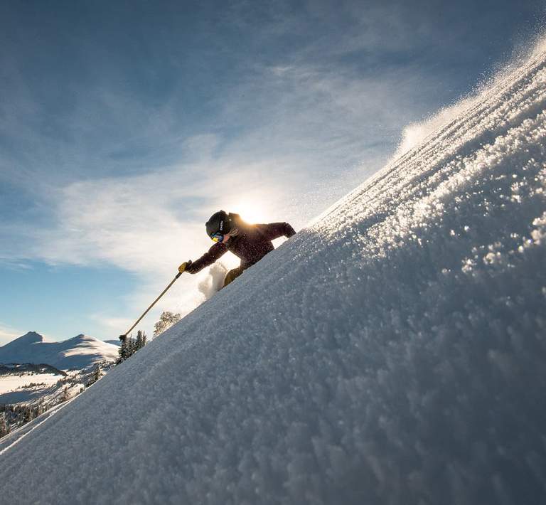 Skier carving their way down untouched snow on the mountain.