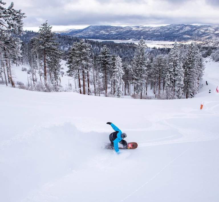 Snowboarder headed downhill with a cloud of powder spraying behind them.