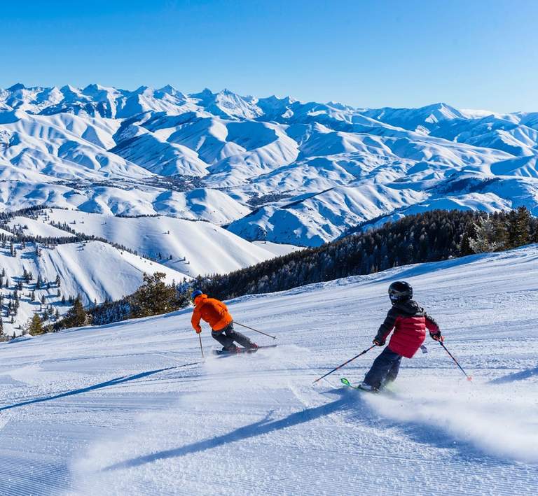 Two people skiing down a groomed ski run