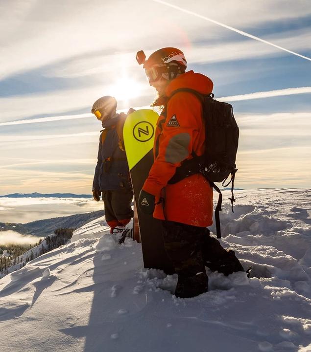Snowboarders standing at the top of a snowy hill