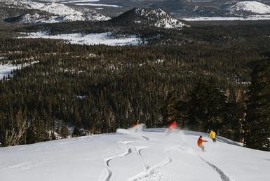 Group of snowboarders maneuvering down a deep snow-covered slope of untouched powder.