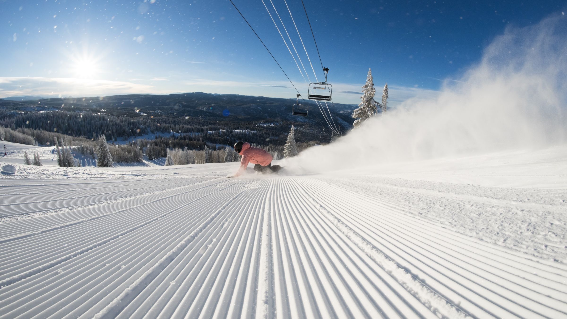 Snowboarder riding on a groomed trail in sunshine.