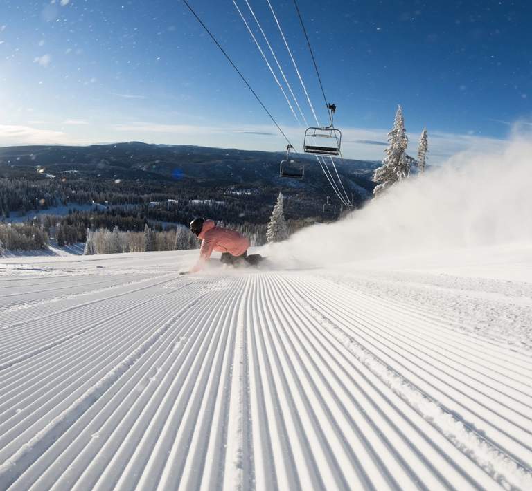 Snowboarder riding on a groomed trail in sunshine.