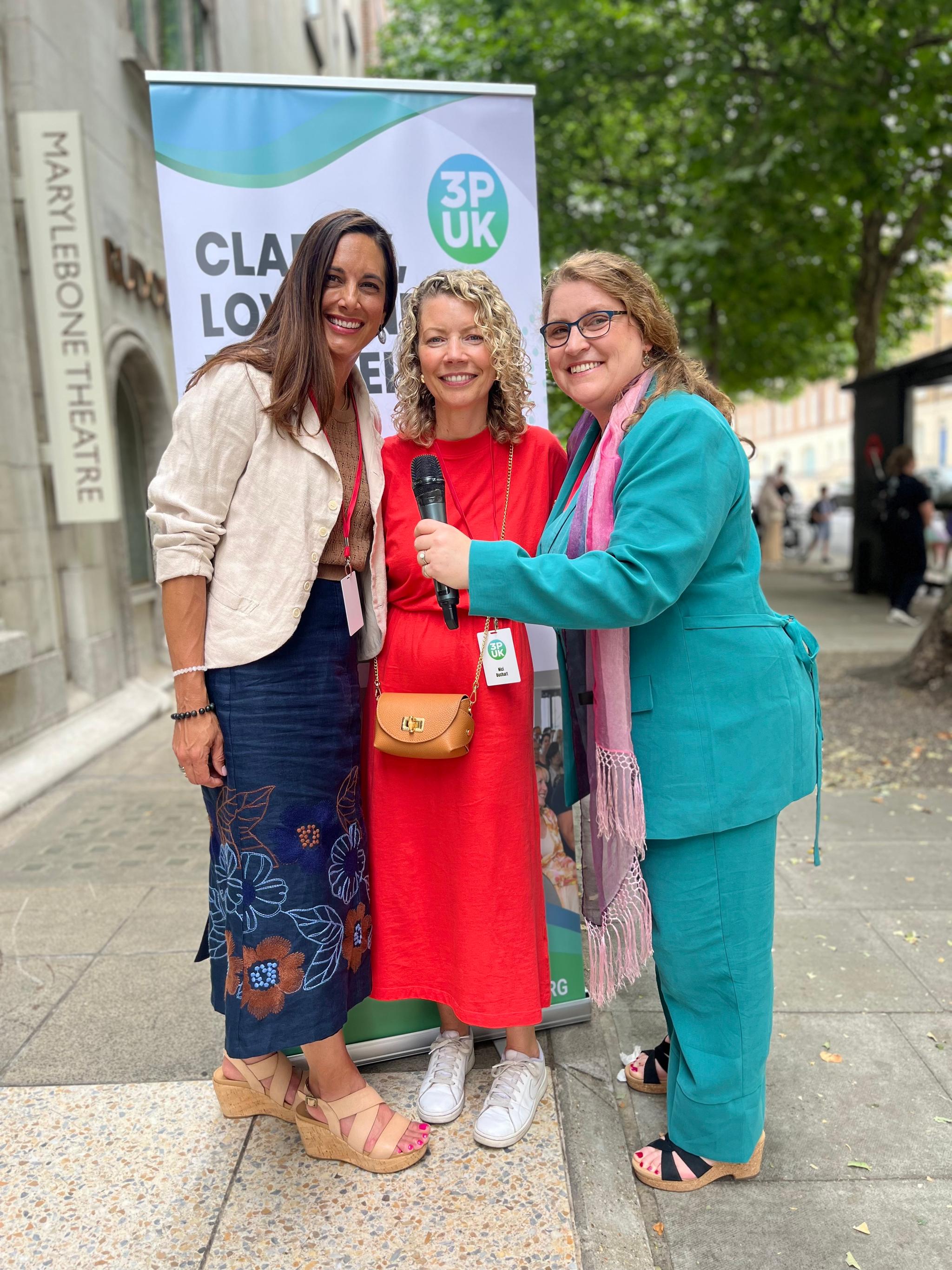 Anita, Nici & Jeanne standing by conference billboard