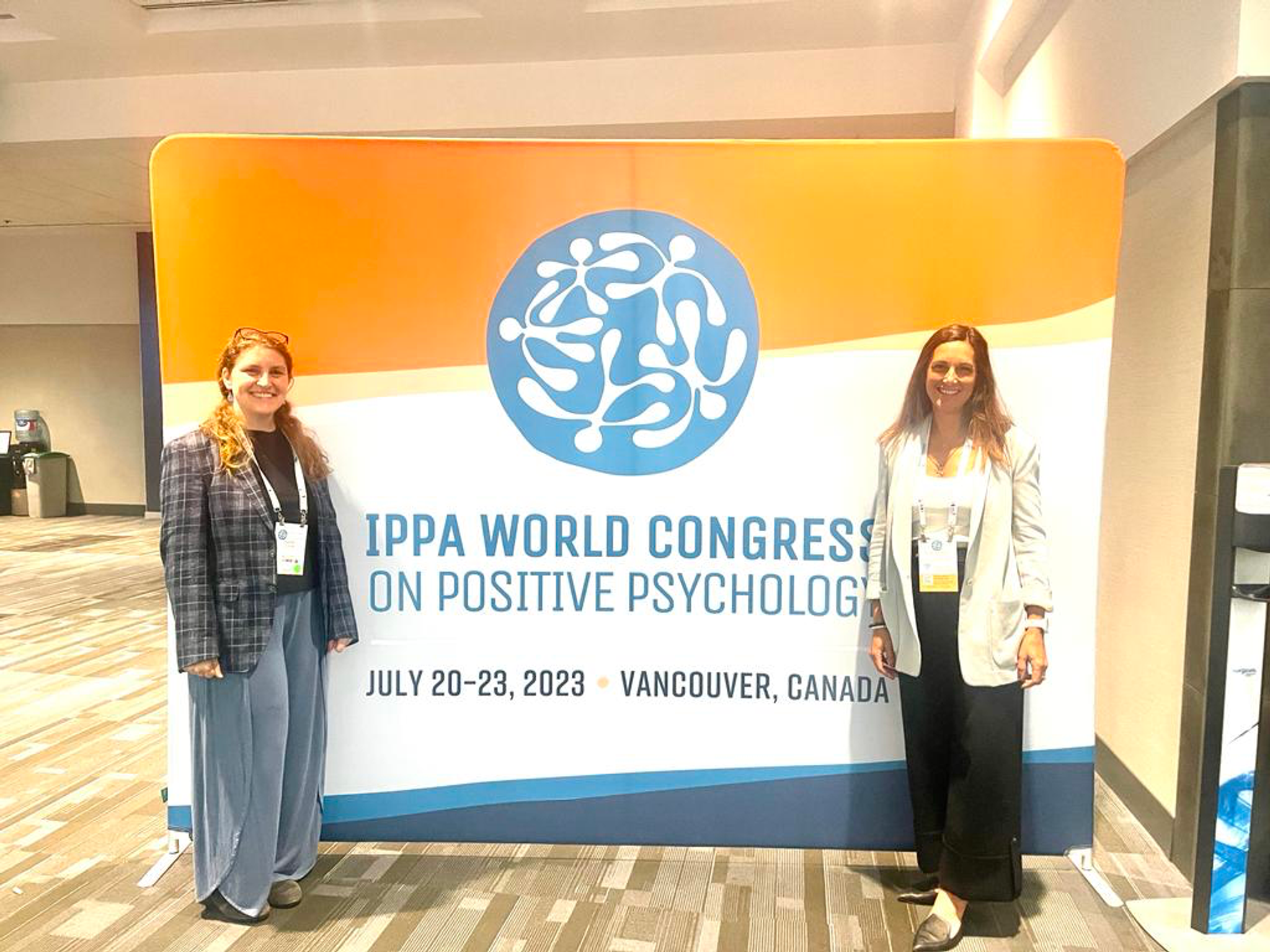 Jeanne COO and Anita CEO standing in front of a conference banner