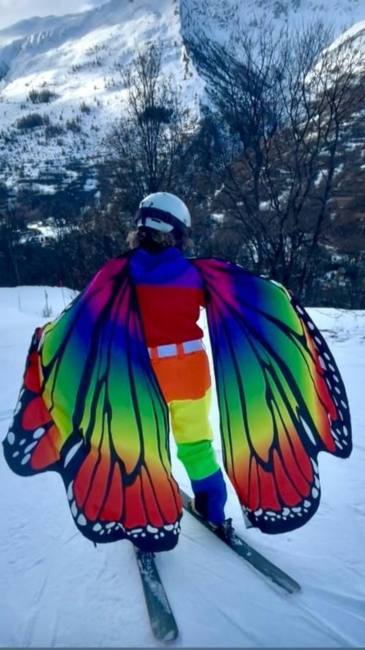 A skier seen from behind wearing large rainbow butterfly wings
