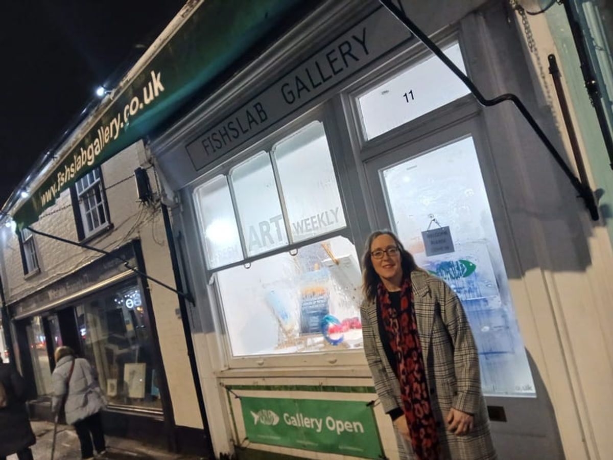 A gallery shopfront at dusk with paintings lit in the window