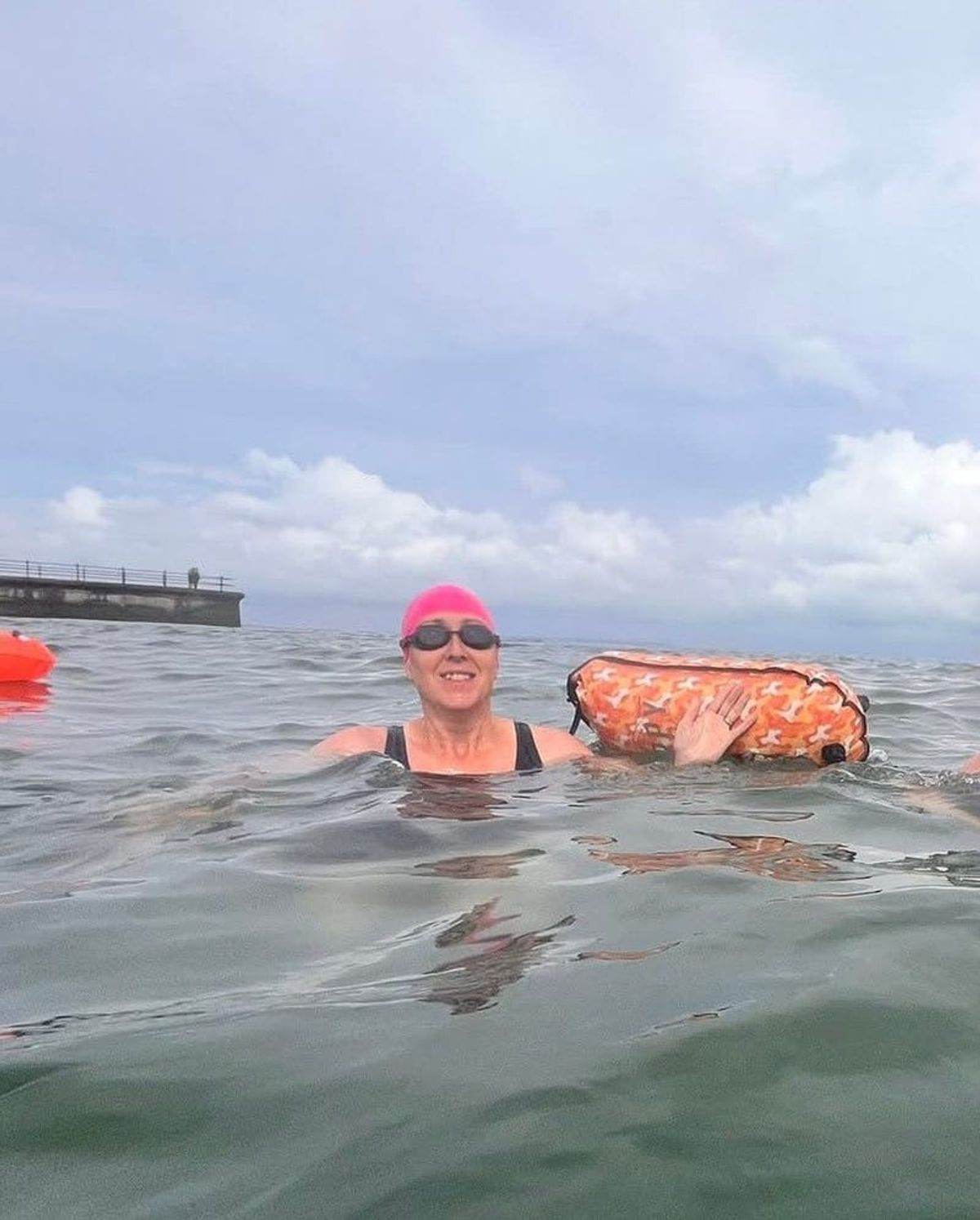A swimmer in a pink cap in open water with a tow float
