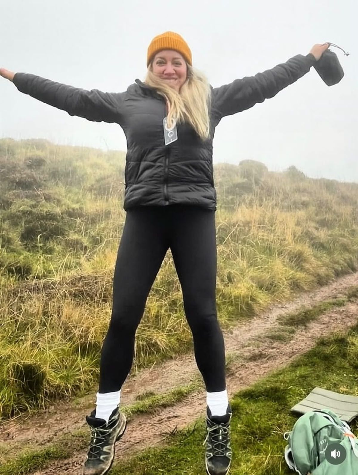 A walker on a grassy hill path with both arms thrown wide