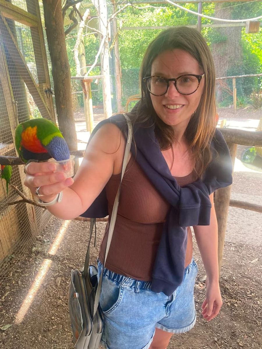 A woman smiling while feeding a lorikeet perched on her hand