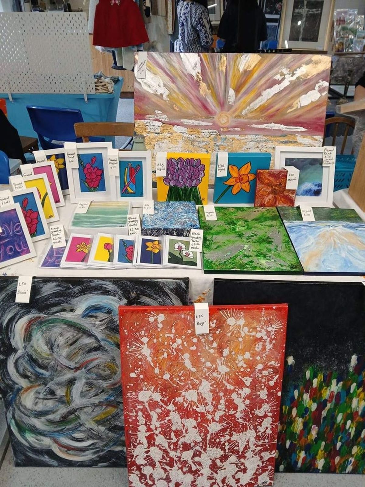 A wall of bright original paintings and printed cards, priced