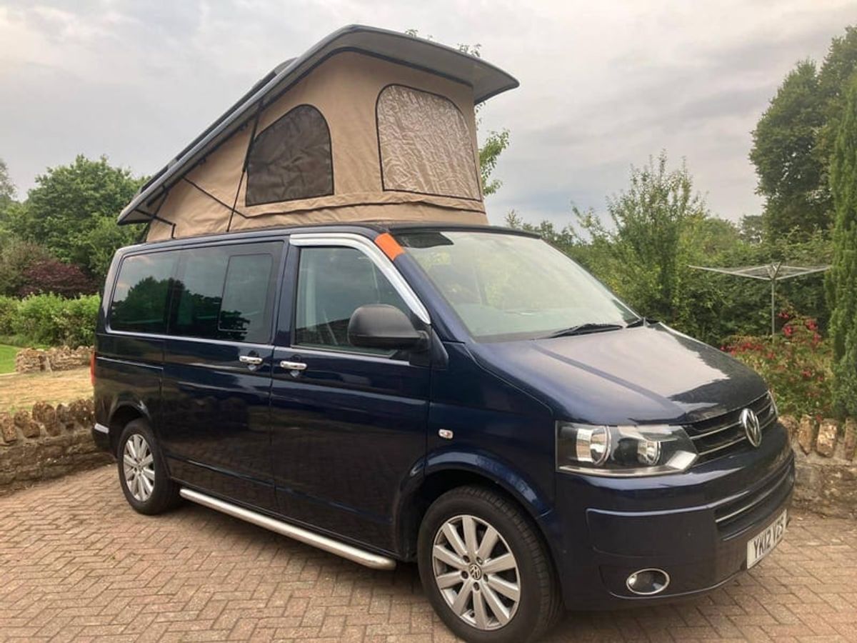 A campervan with its roof popped, parked on grass